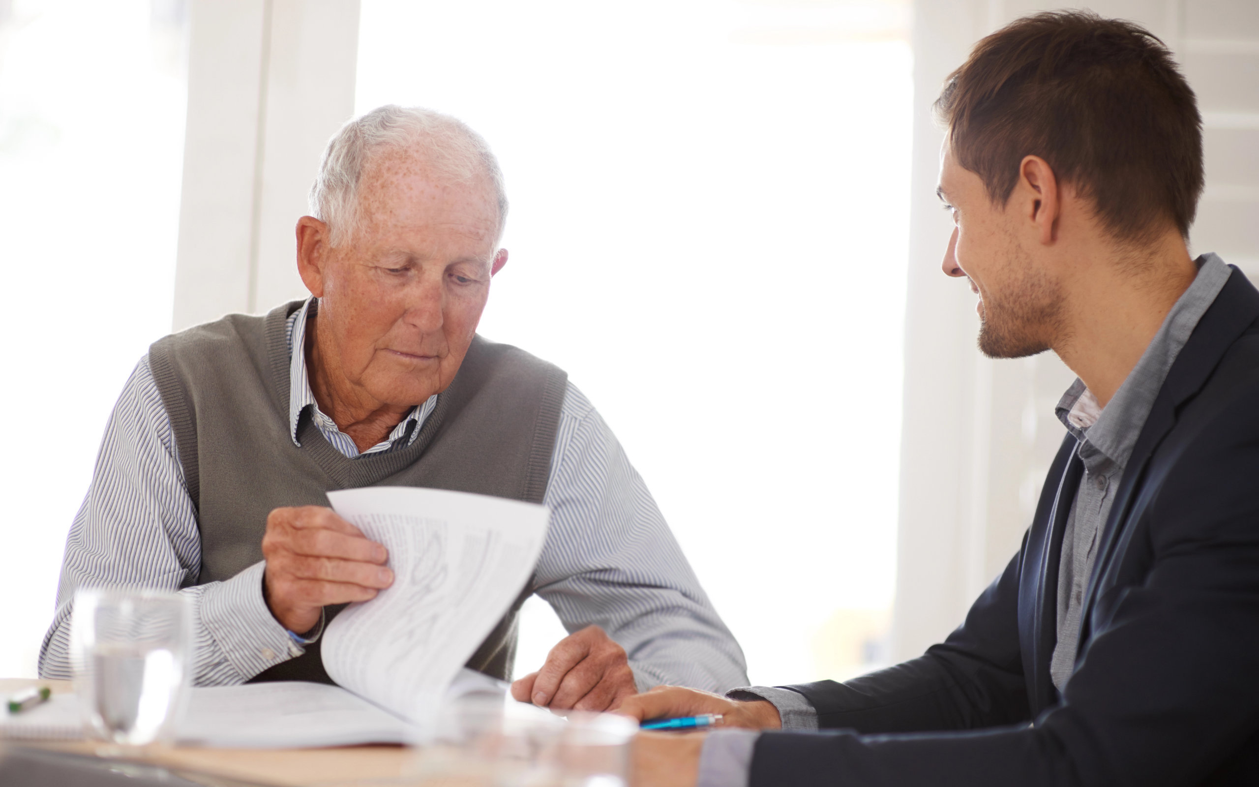 An elderly and young man sitting at a table looking at paperwork